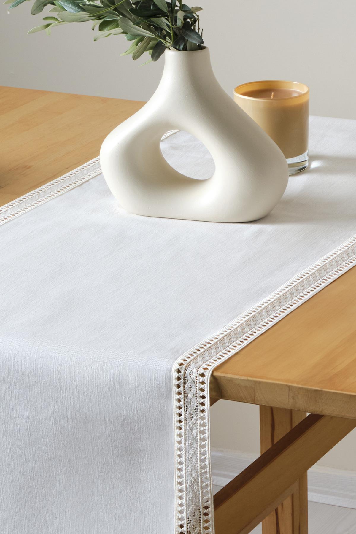 Dantelli beyaz runner, ahşap masa üzerinde modern vazo ve mum ile dekoratif sunum